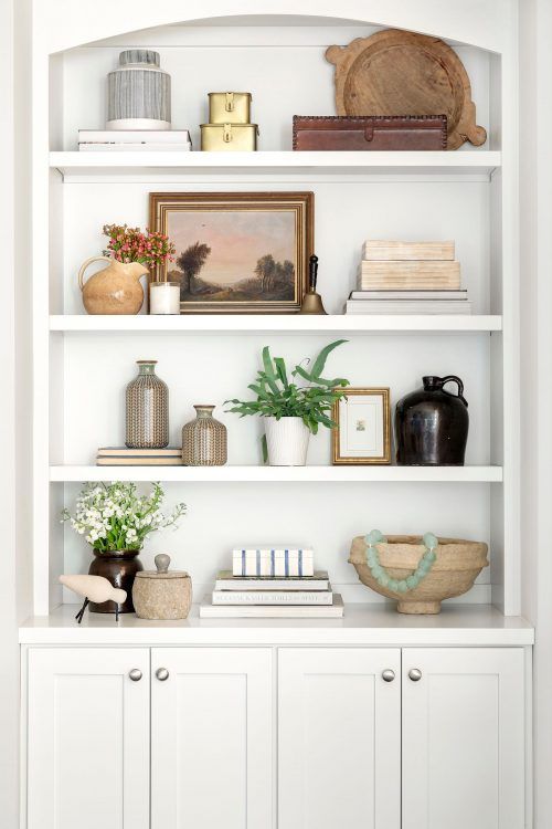 a white bookcase filled with lots of books and vases on top of it