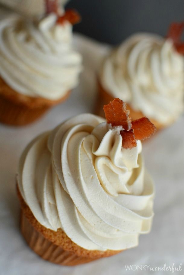 three cupcakes with white frosting and bacon on top are sitting on a table