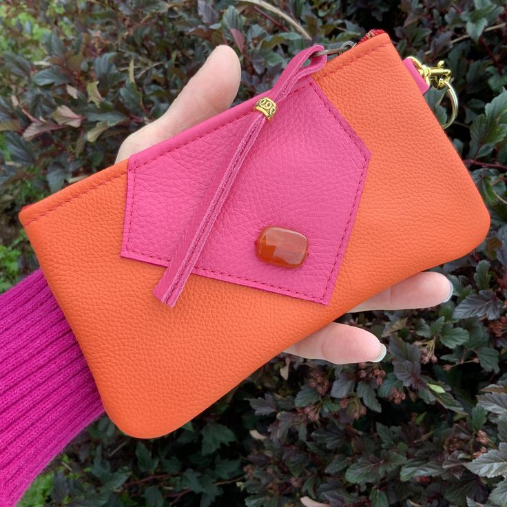 a person holding an orange and pink purse with a tag on it's side