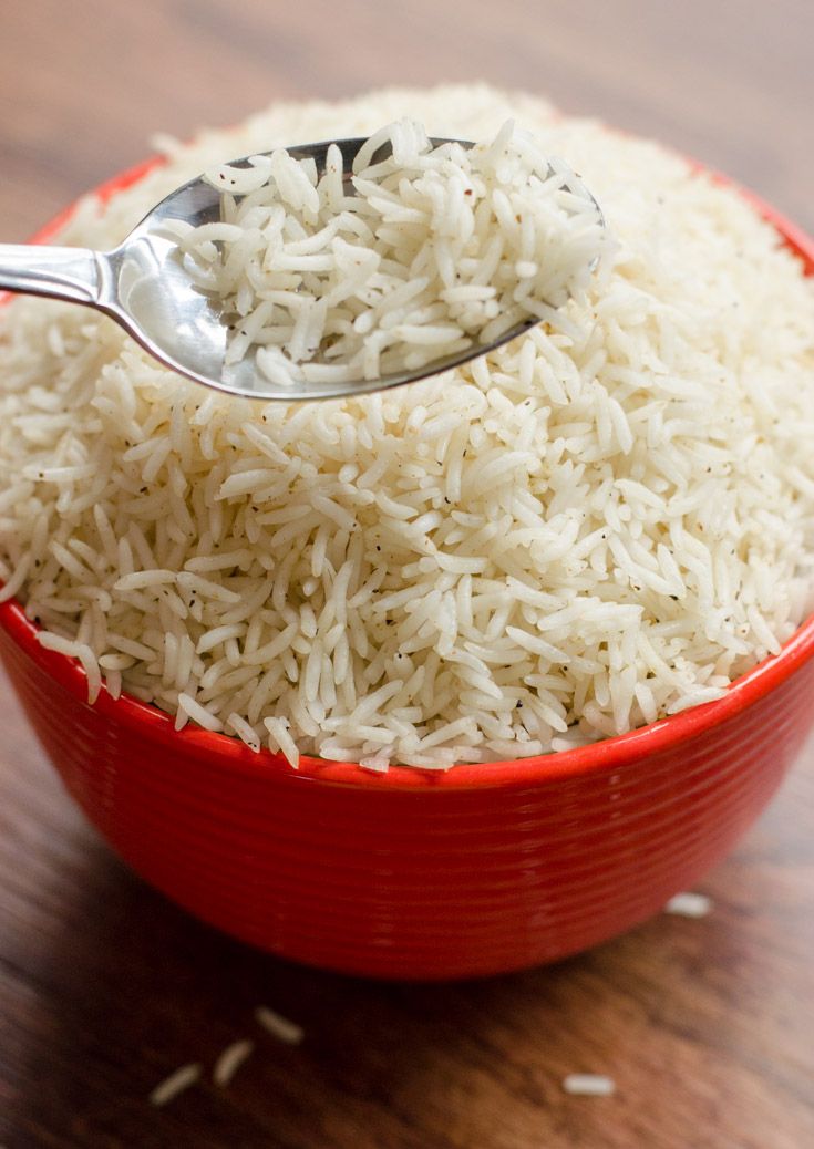 a red bowl filled with white rice and a silver spoon in it on a wooden table