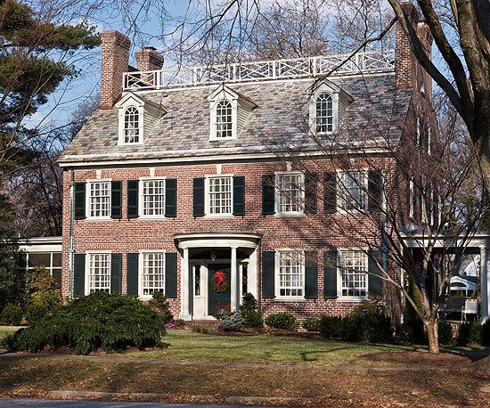 a large brick house with white trim and black shutters on the front, surrounded by trees