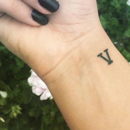 a woman's wrist with a small black v tattoo on her left arm and the letter v tattooed on it