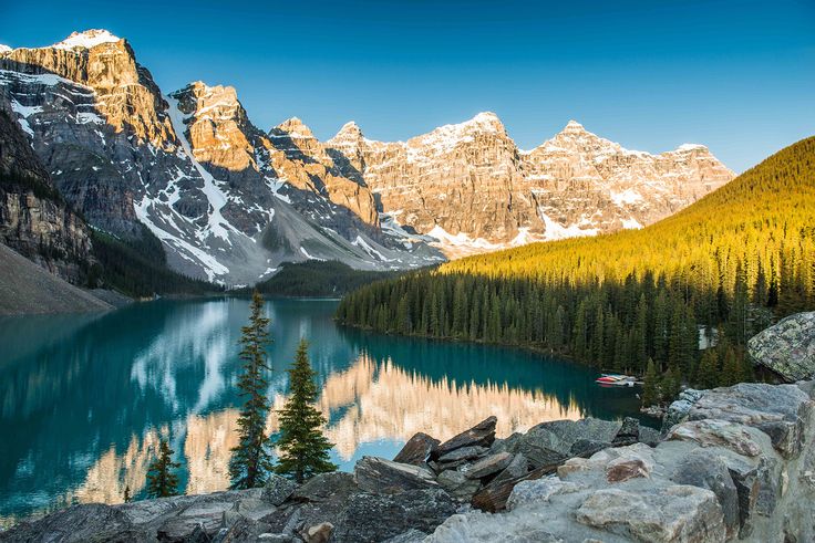 a lake surrounded by mountains and trees in the foreground with rocks on both sides