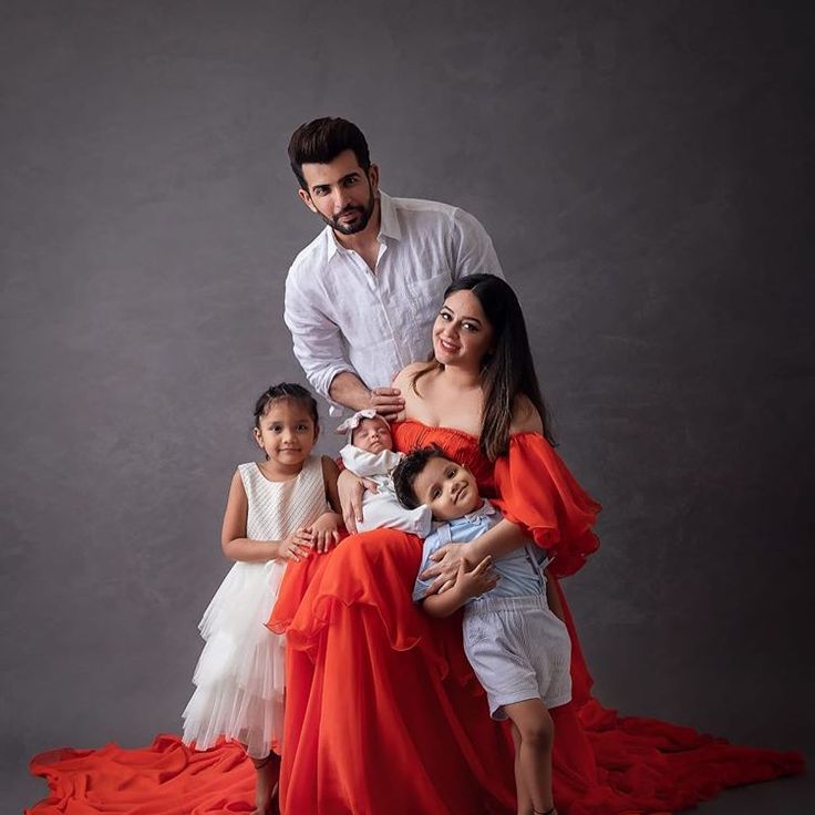 a man is posing with two children and an infant in front of him on a red blanket