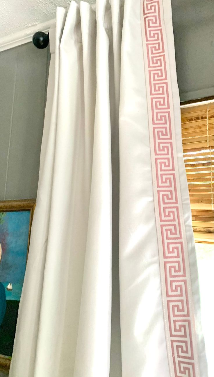 white curtains with pink greek border hanging on the side of a window in a room