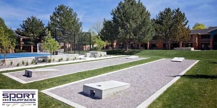 an empty basketball court in the middle of a grassy area with benches and trees around it