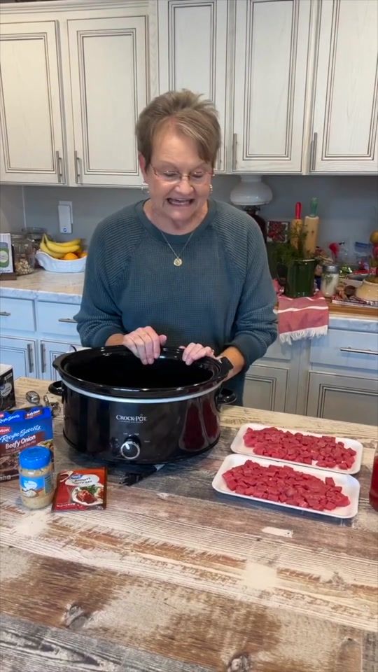 a woman standing in front of a crock pot filled with meatballs and vegetables