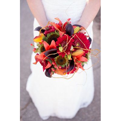 a woman in a white dress holding a red and orange bouquet on her wedding day