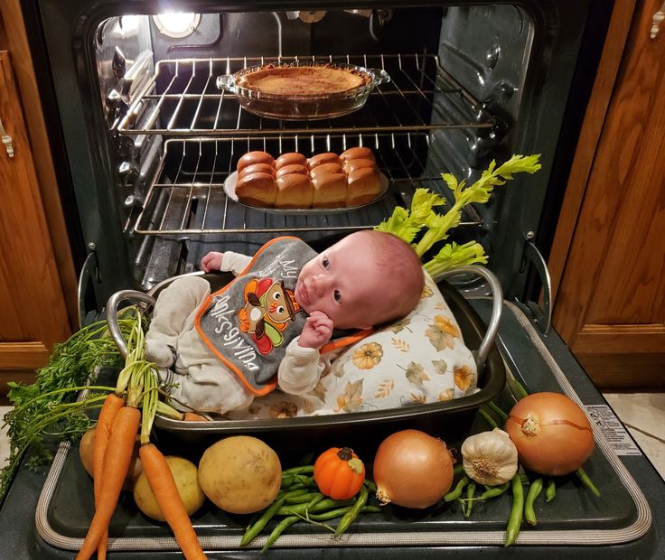 a baby laying in an oven with vegetables and bread on the rack next to it