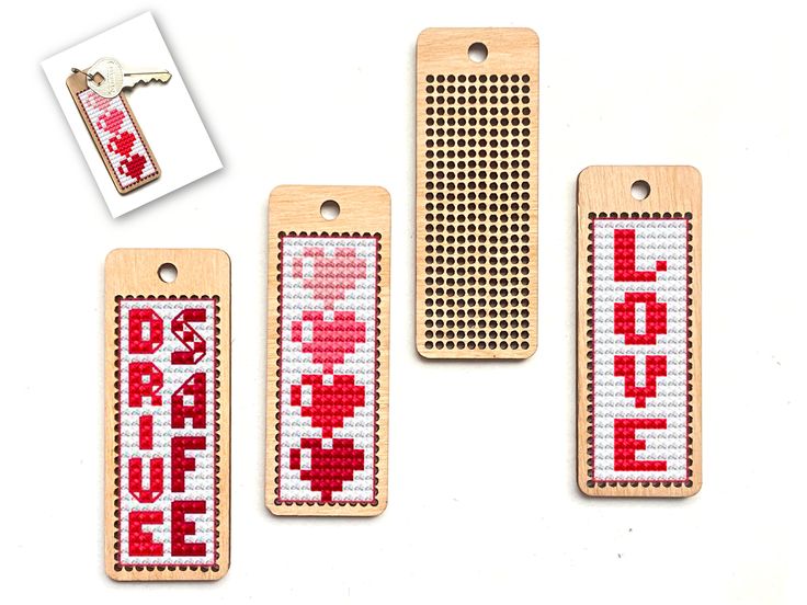 three wooden tags with cross stitch designs on them, one is red and the other has white