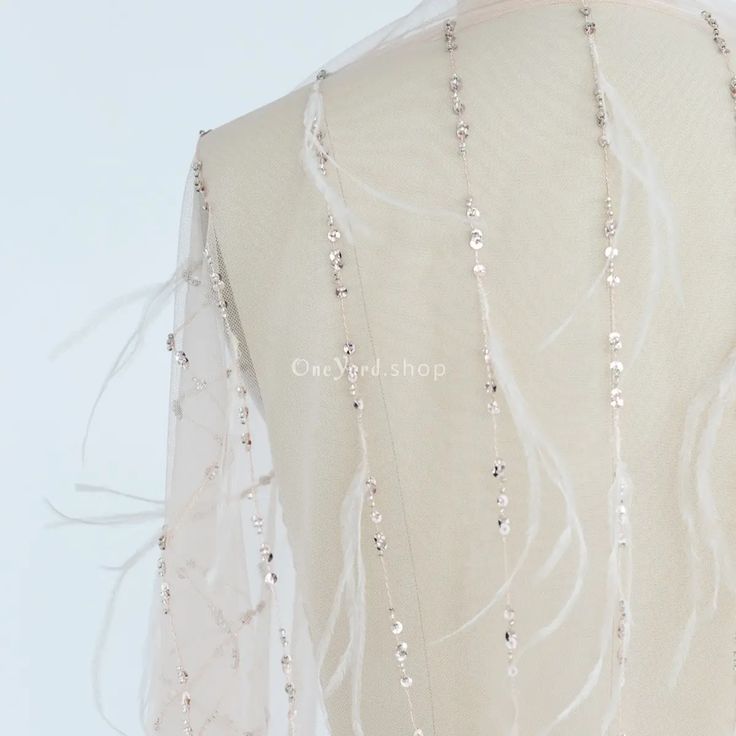 the back of a woman's white dress with beads on it and sheer fabric