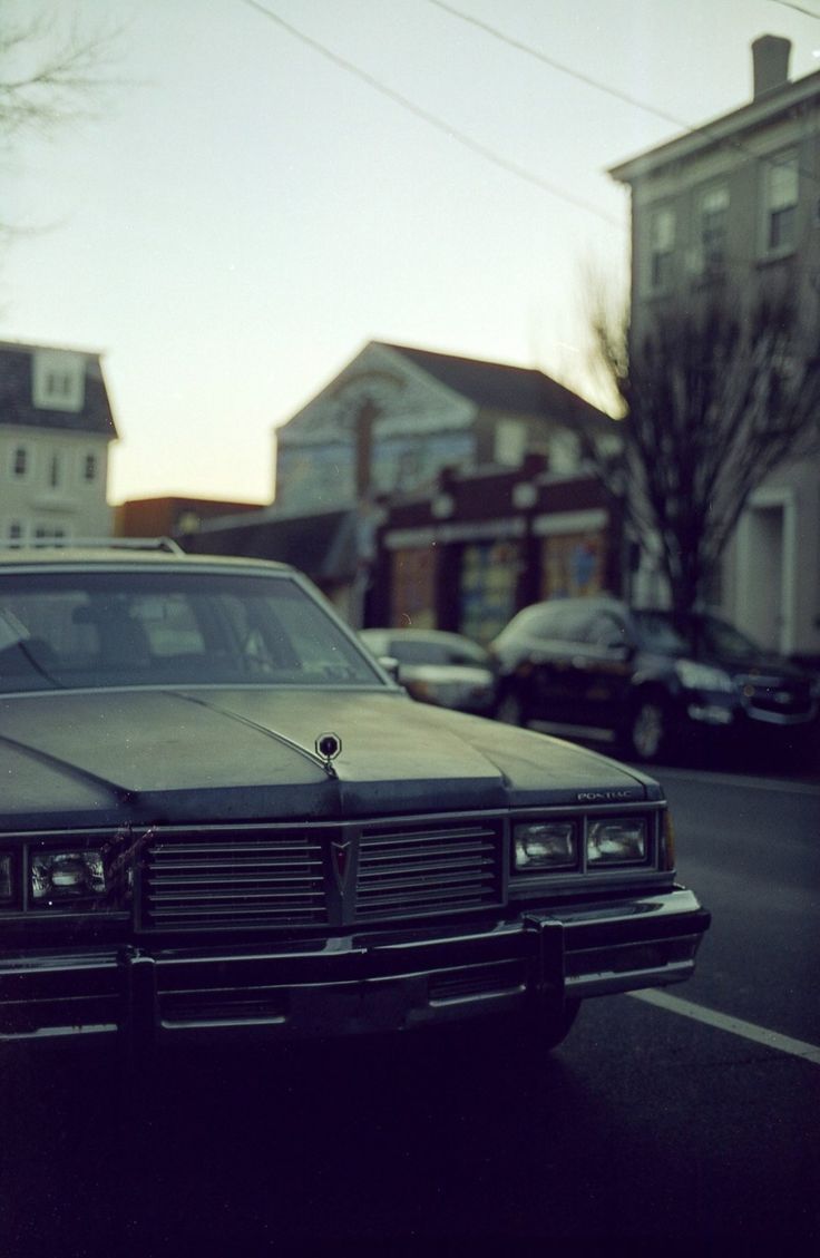 an old car is parked on the side of the road in front of some houses