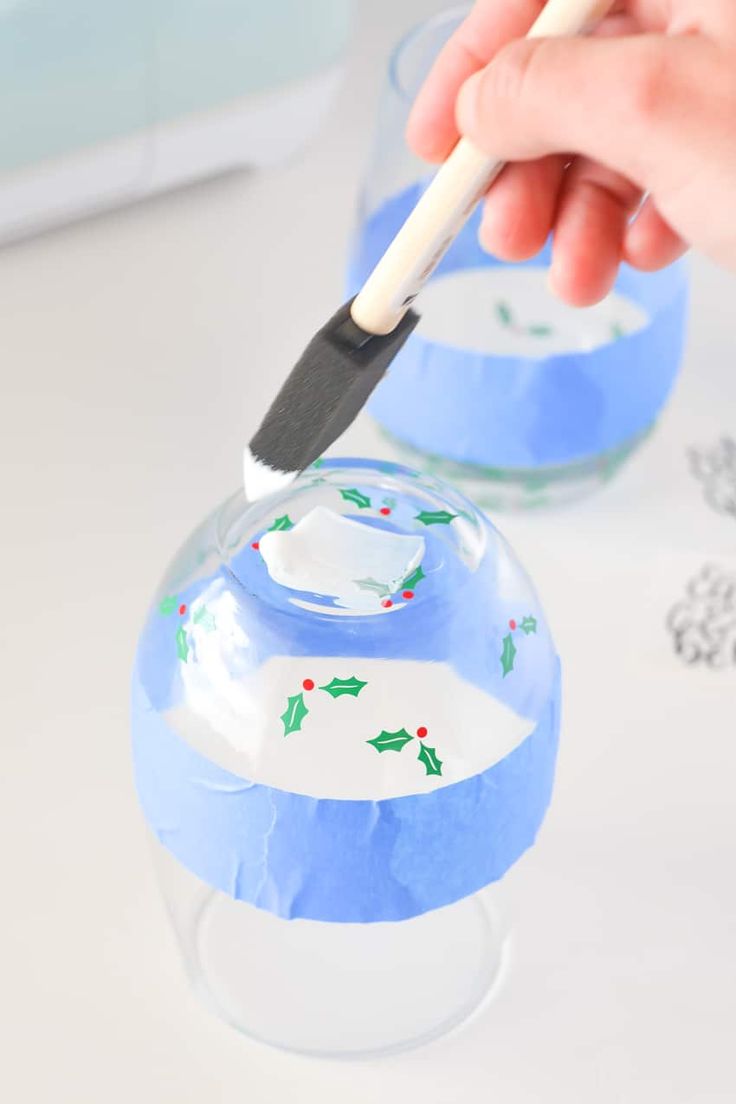 a hand is holding a paintbrush and painting the inside of a glass jar with frosting on it