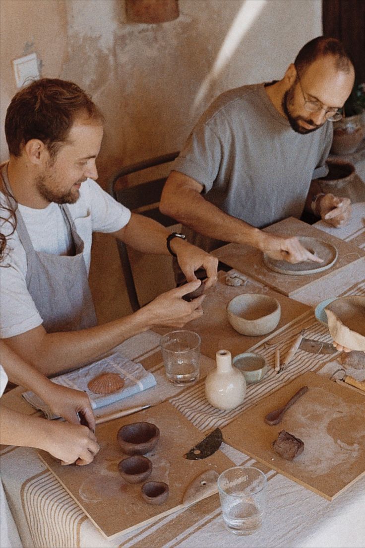 two men sitting at a table making doughnuts