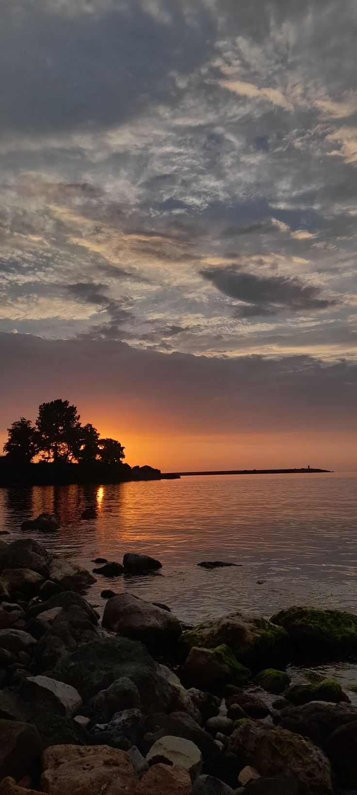 the sun is setting over an island in the middle of the ocean with rocks on it