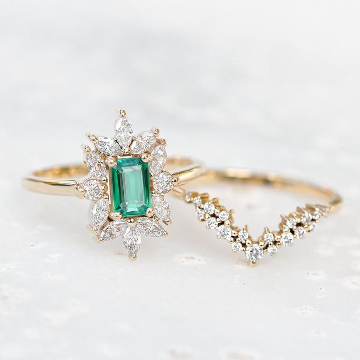 two gold rings with an emerald and diamond ring on top, one in the shape of a v