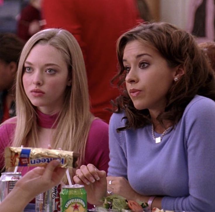 two women sitting at a table with food in front of them and one woman holding a sandwich