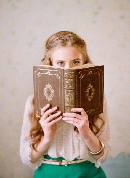 a woman is holding an open book in front of her face