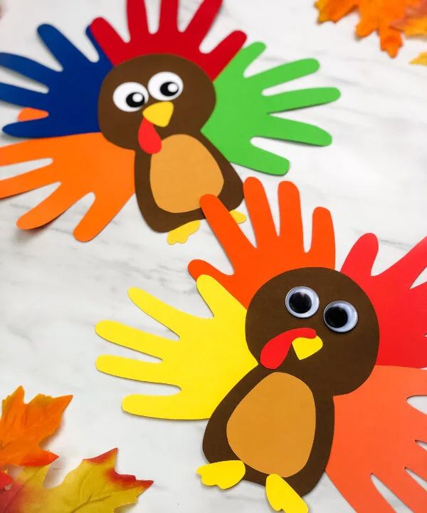 two turkey hand puppets sitting on top of a white table with autumn leaves around them