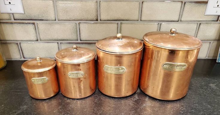 three gold canisters sitting next to each other on a counter in front of a brick wall