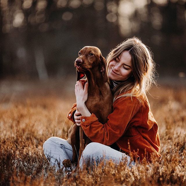 a woman sitting in the grass holding a brown dog with her face close to her chest