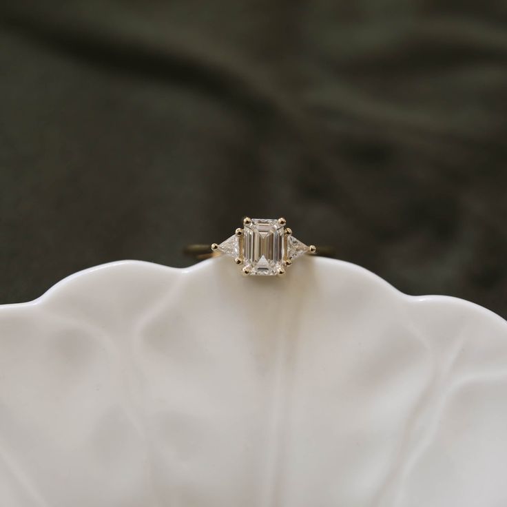 an emerald cut diamond ring sitting on top of a white flowered cloth covered napkin