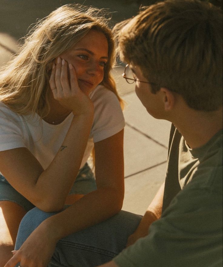 a woman sitting on the ground talking to a man who is holding his hand up to his face