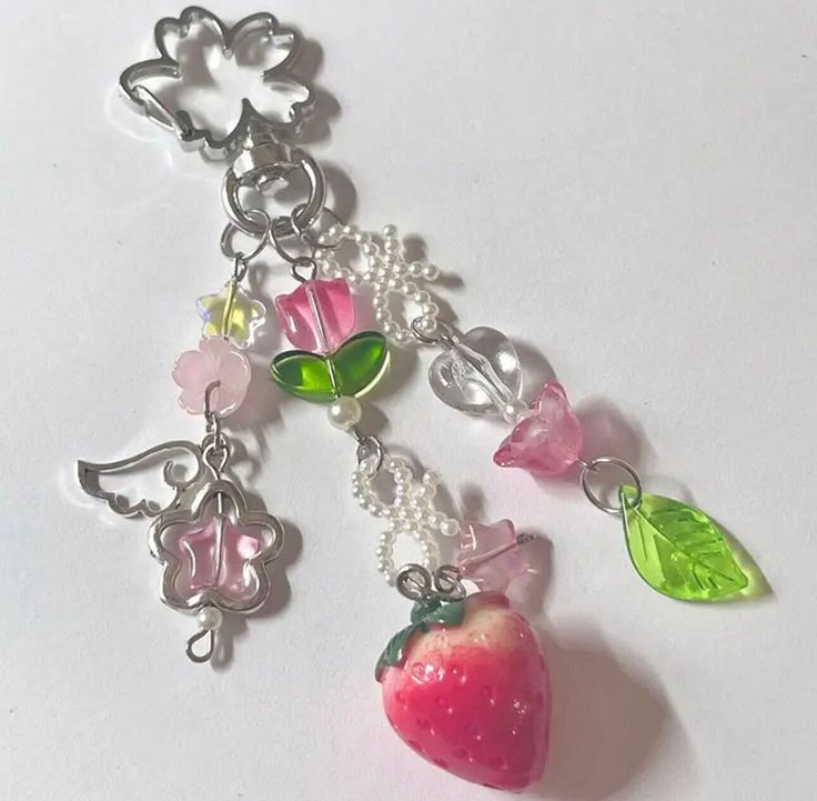 an apple charm is hanging from a chain on a white surface with flowers and leaves