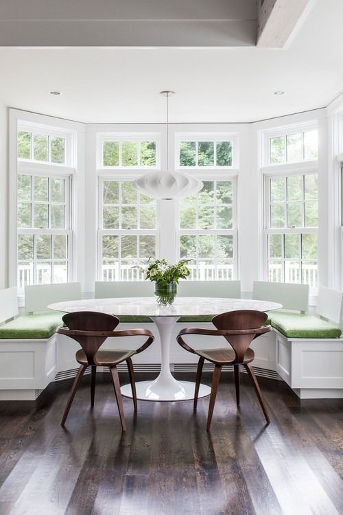 a dining room table with two chairs and a bench in front of the bay window