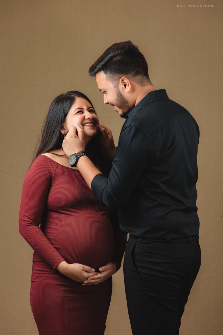 a pregnant woman standing next to a man in a black shirt and red dress with his hand on her belly