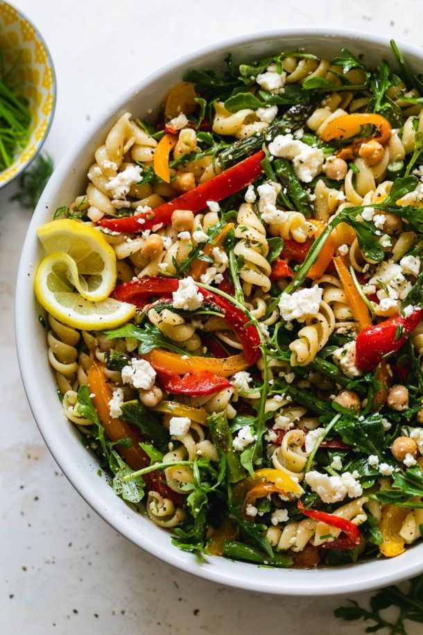 a white bowl filled with pasta salad and topped with feta cheese, red peppers, bell pepper, and green onions