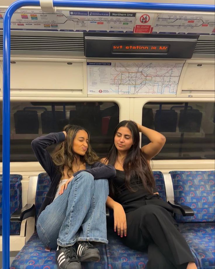 two young women sitting on a train looking at the camera with their hands behind their heads