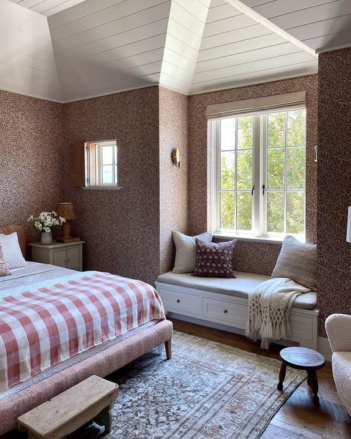 a bed sitting under a window in a bedroom next to a chair and ottoman on top of a rug