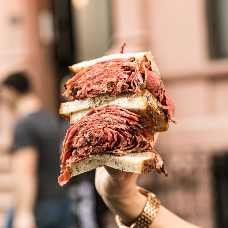 a person holding up two halves of a sandwich in front of them with meat on it