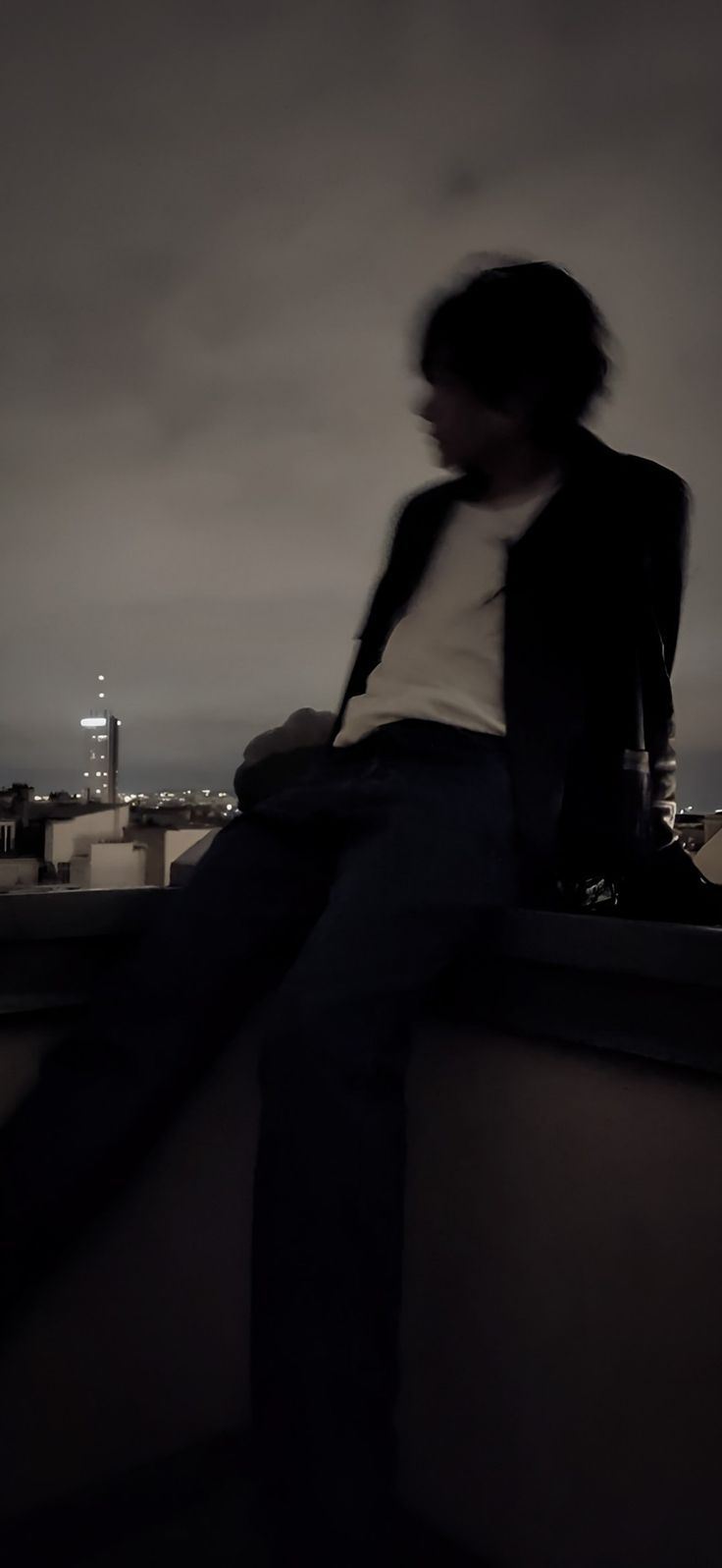 a man sitting on top of a roof next to a tall building with a city skyline in the background