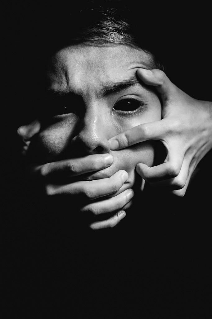 a black and white photo of a person covering their face with his hands in the dark