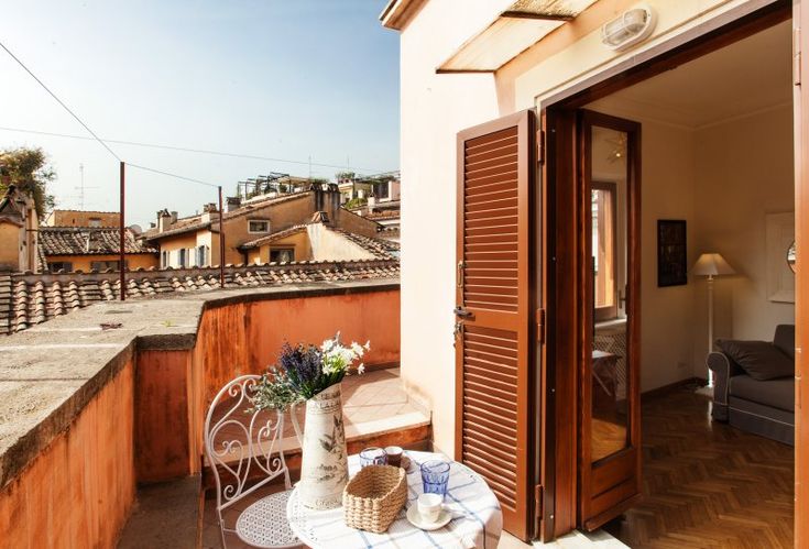 an open door to a balcony with a table and chairs on the outside, overlooking rooftops