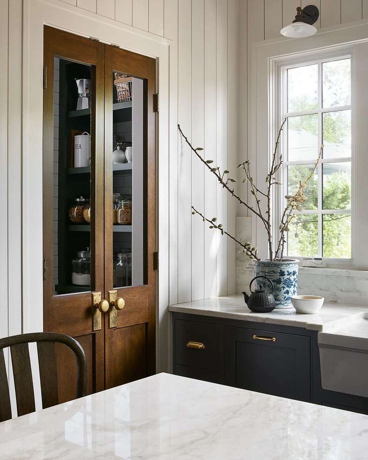 a kitchen with white counter tops and black cabinetry next to a wooden pantry door