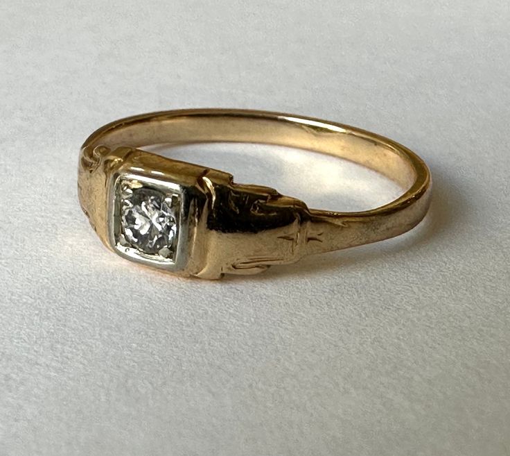 an old yellow gold ring with a single diamond in the center, sitting on a white surface