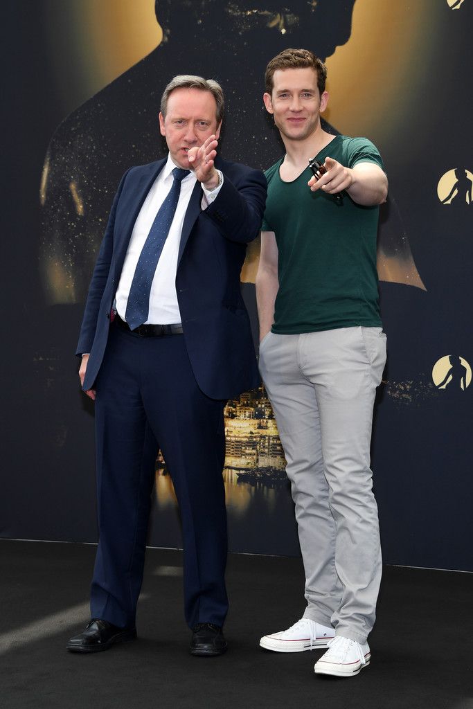 two men standing next to each other in front of a wall with an image on it