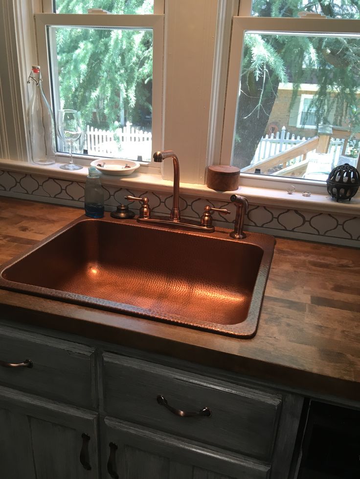 a kitchen sink sitting under a window next to a wooden counter top in front of two windows