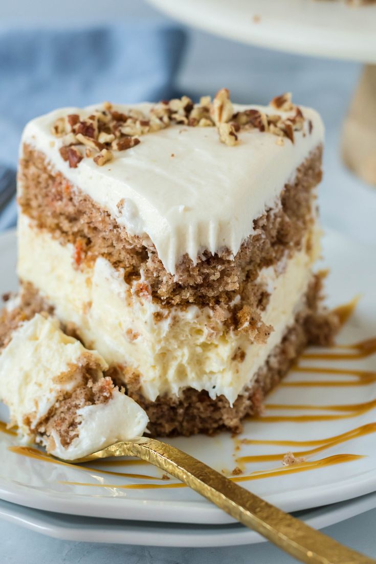 a slice of carrot cake with white frosting and nuts on top, sitting on a plate next to a fork