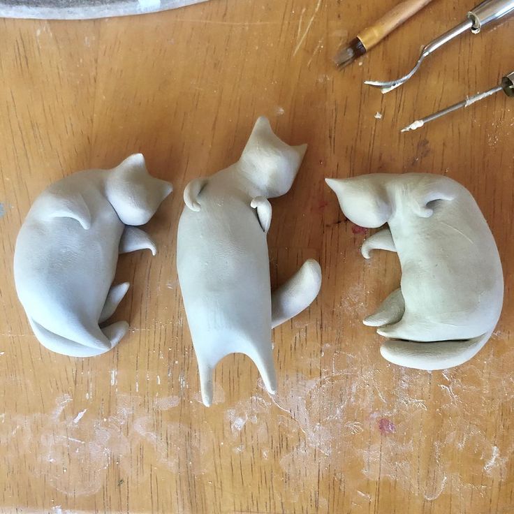 three clay cats sitting on top of a wooden table