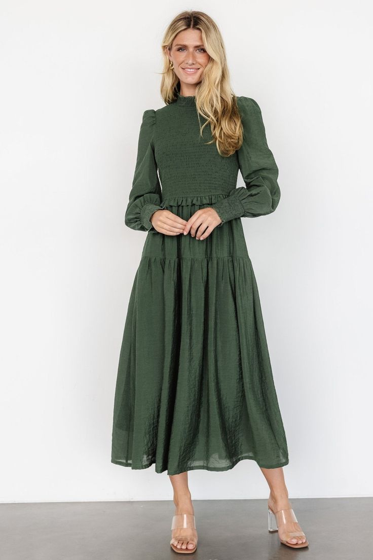 The Daria Smocked Maxi Dress in Juniper Green is a darling choice for any occasion, featuring a shirred mock neckline, smocked bodice, and puffed sleeves with shirred cuffs. This fully lined dress includes a delicate ruffle at the waist, a single tier at the top of the skirt, and unlined sleeves for a touch of elegance. Green Puff Sleeve Dress With Smocked Bodice, Fitted Midi Dress With Smocked Bodice And Bishop Sleeve, Fitted Long Sleeve Dark Green Midi Dress, Fitted Dark Green Long Sleeve Midi Dress, Dark Green Fitted Long Sleeve Midi Dress, Ruched Lantern Sleeve Midi Dress For Fall, Green Midi Smocked Dress With Smocked Cuffs, Fitted Smocked Dress With Elastic Sleeves For Fall, Long Sleeve Smocked Dress With Ruched Detail