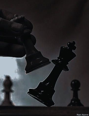 a hand holding a black chess piece next to a white and black pawn on a chess board