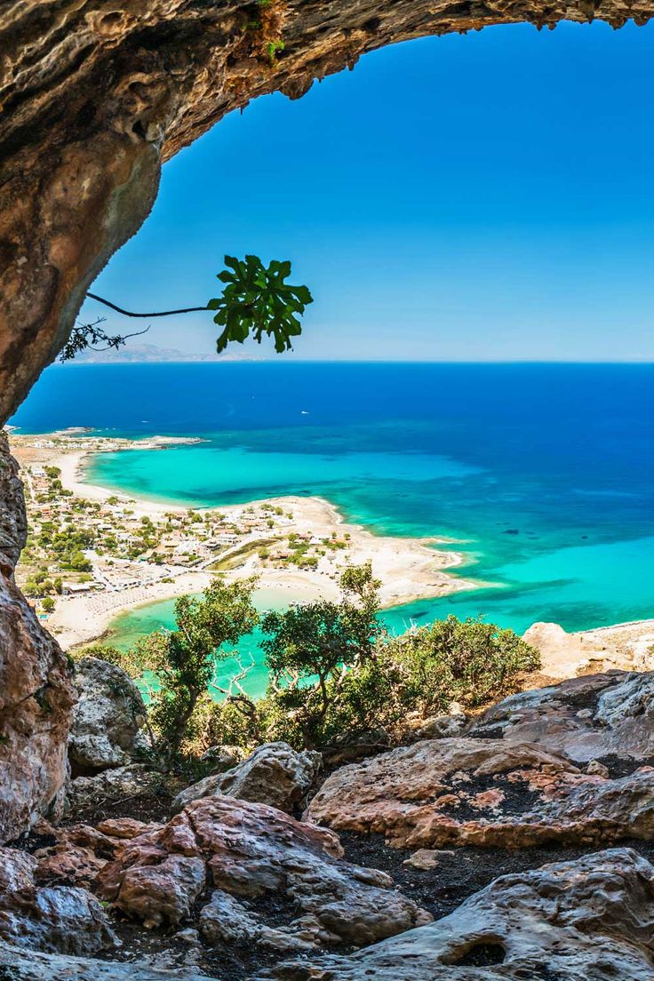 the view from inside a cave looking out at an ocean and sandy beach with blue water