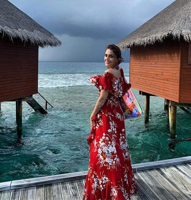 a woman in a red dress standing on a dock next to some water and thatched huts