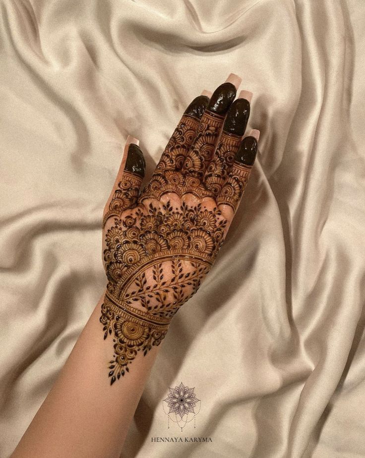 a woman's hand with henna on top of white sheets and satin material