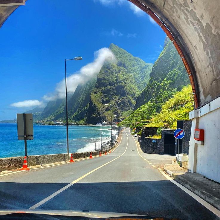 the view from inside a vehicle looking out at mountains and blue water in the ocean