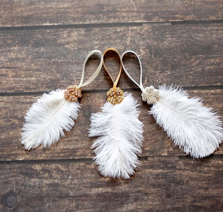 three white feathers with gold accents hang on a wooden surface, one is hanging from a hook